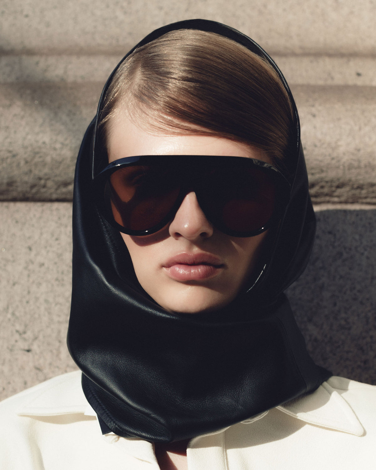 Model in a black leather hood wearing Past Midnight The Icon Black oversized sunglasses with amber lenses
