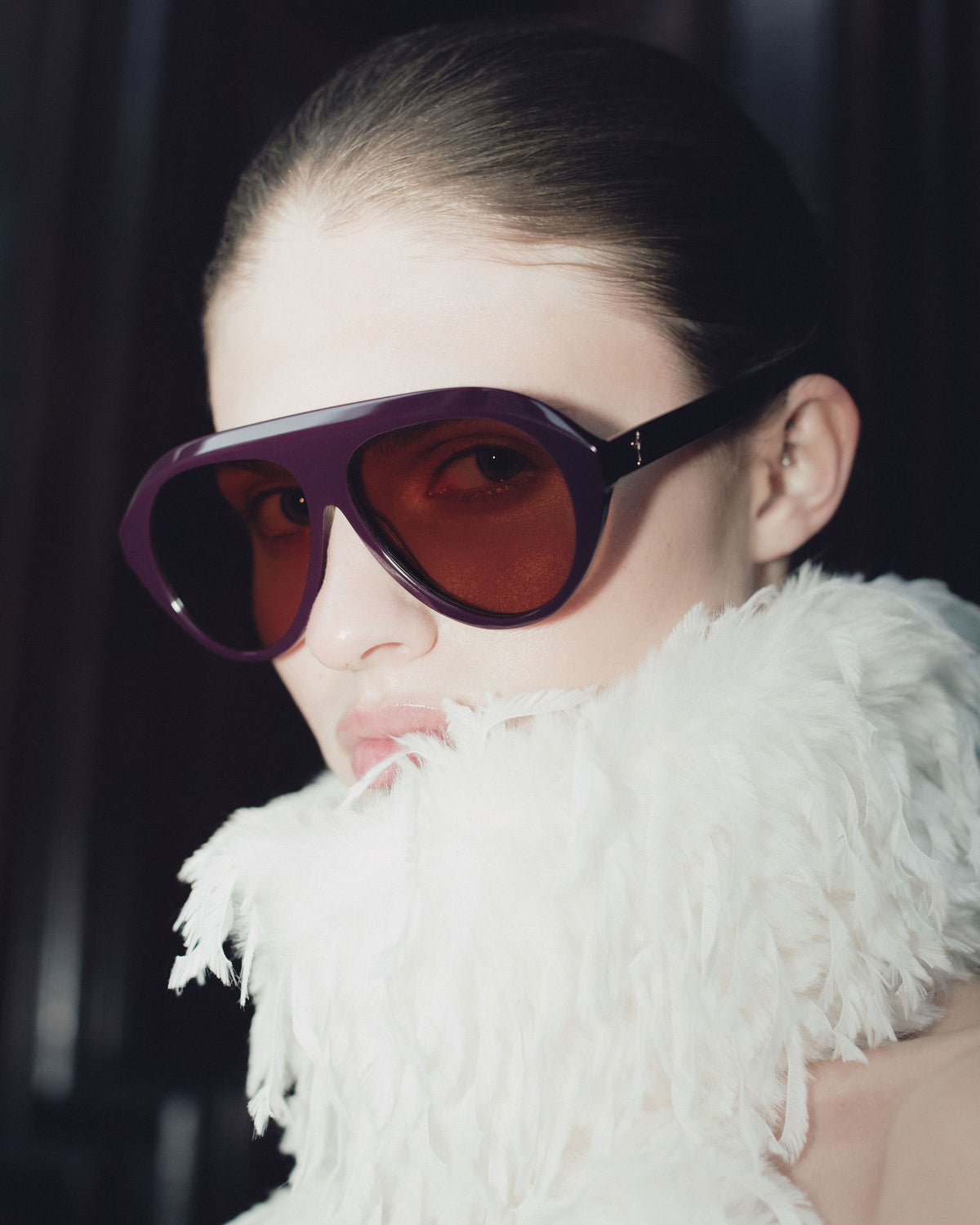 Model in Past Midnight The Icon Retrofête Violette sunglasses with amber lenses and a white feather collar