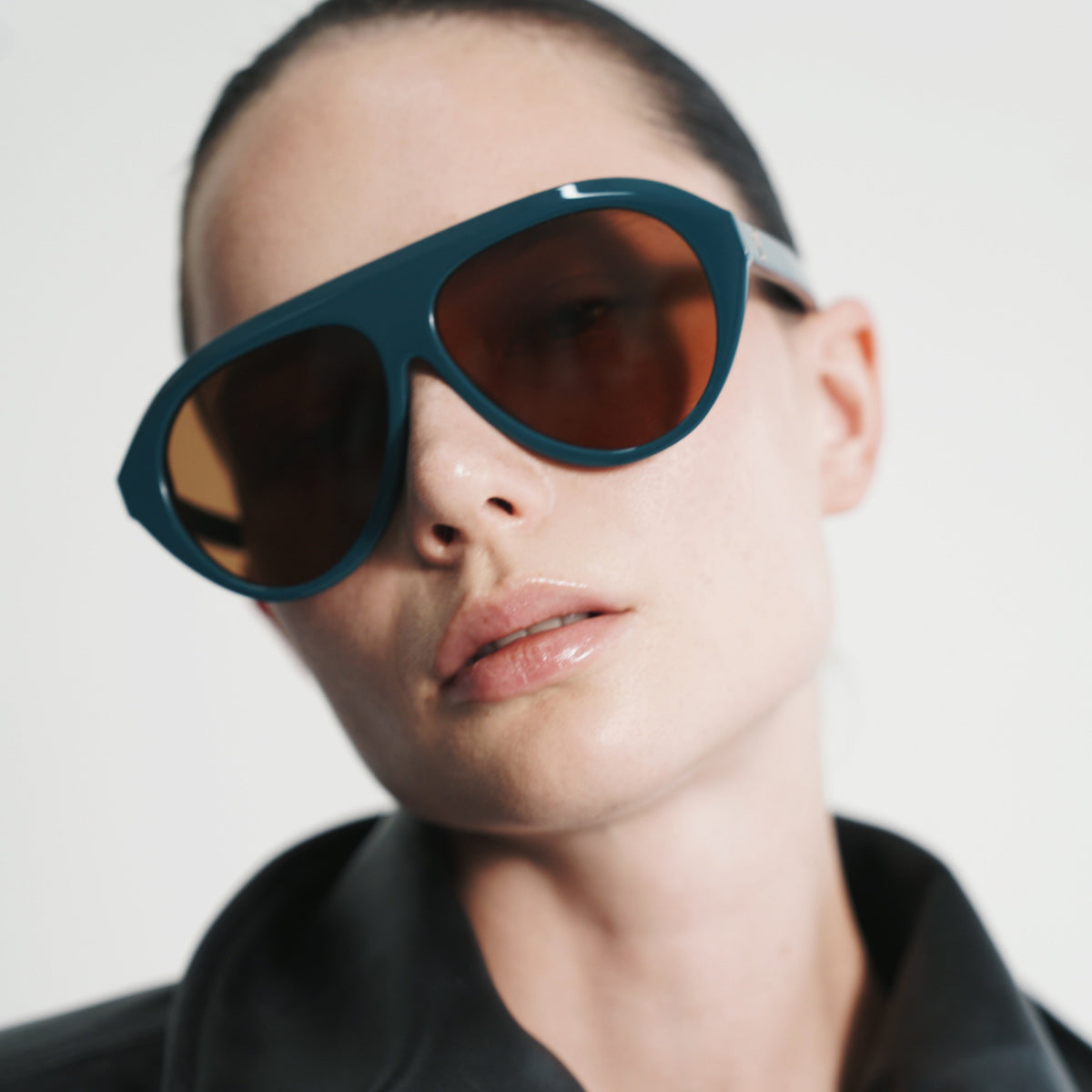 Tilted portrait in Retrofête x Past Midnight The Icon Sarcelle teal shield sunglasses with amber lenses