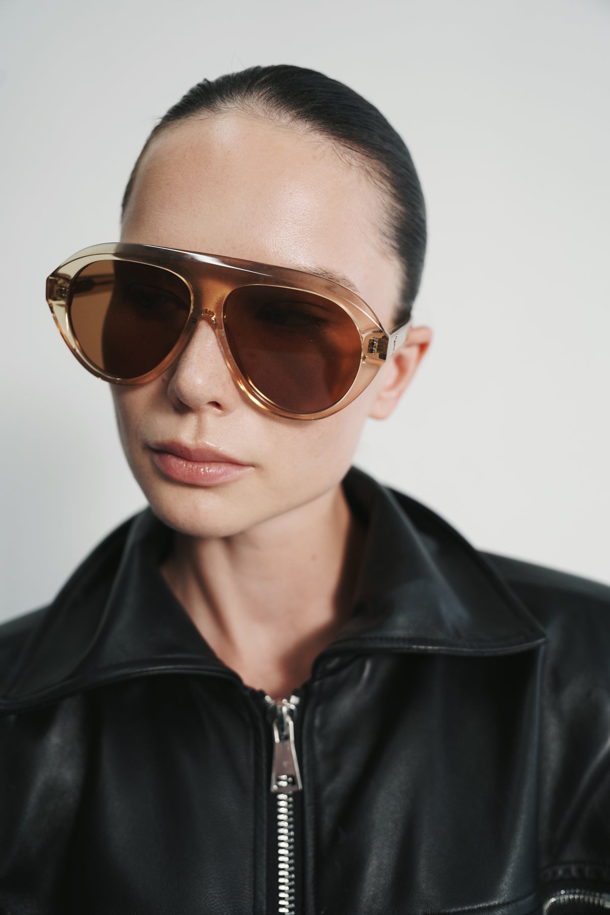 Model in a black leather jacket wearing Retrofête x Past Midnight The Icon Ochre translucent honey sunglasses with amber lenses
