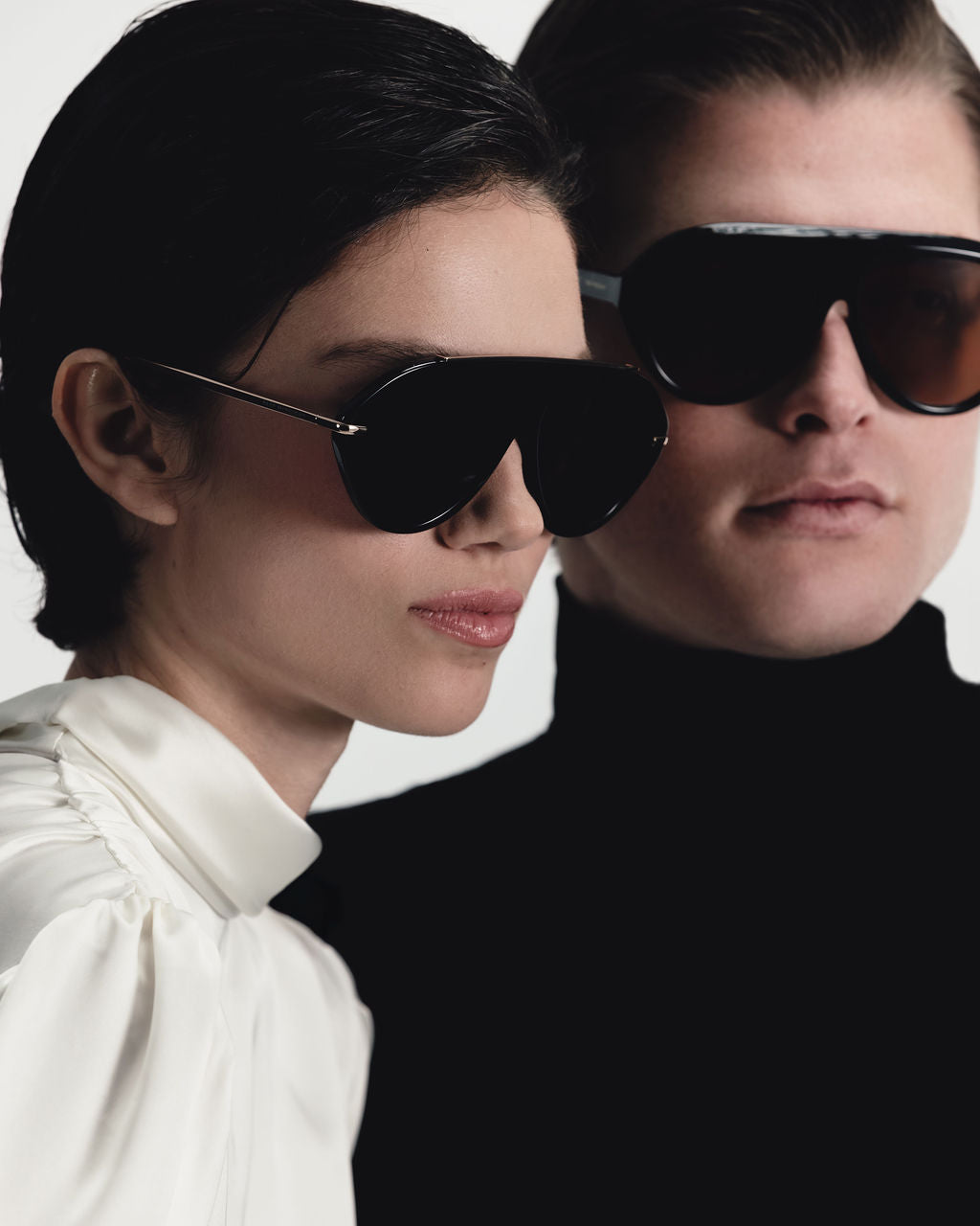 Couple in ivory and black wearing Past Midnight black sunglasses, side by side